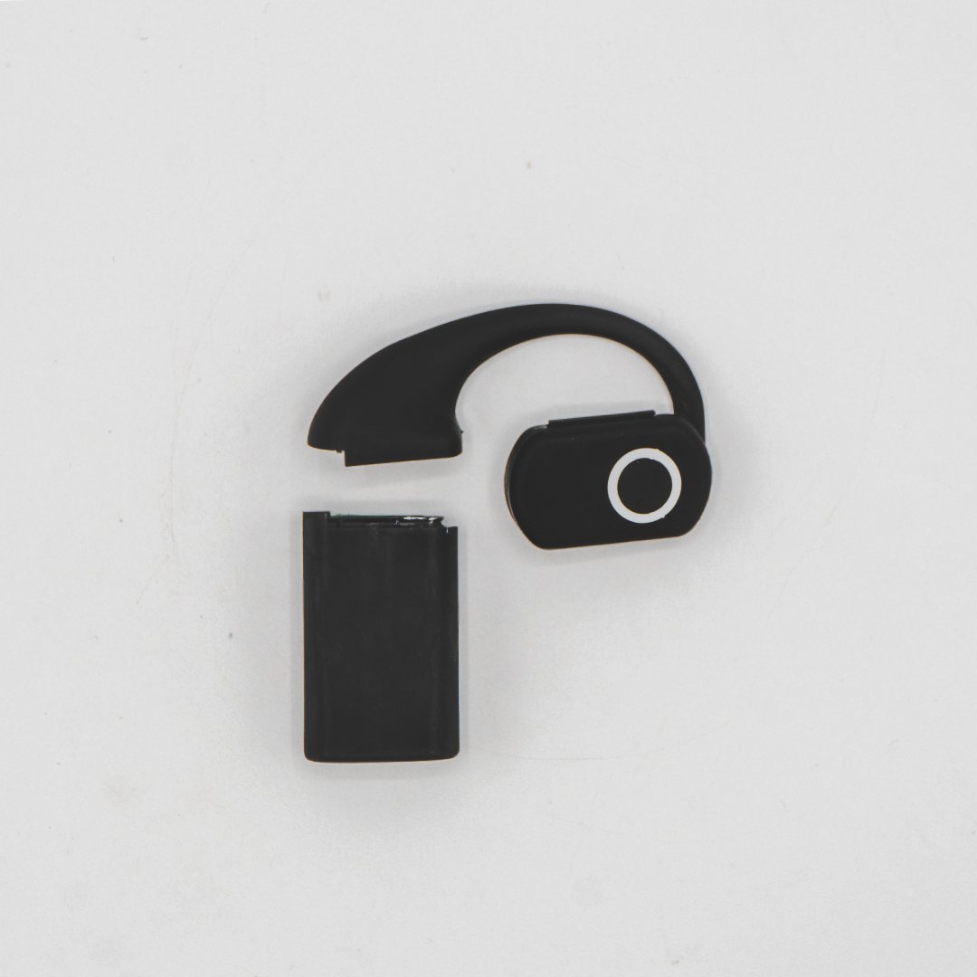 The QuickComm Earpiece photographed from above: the over-ear hook and round control pod, with a battery pack detached beside it